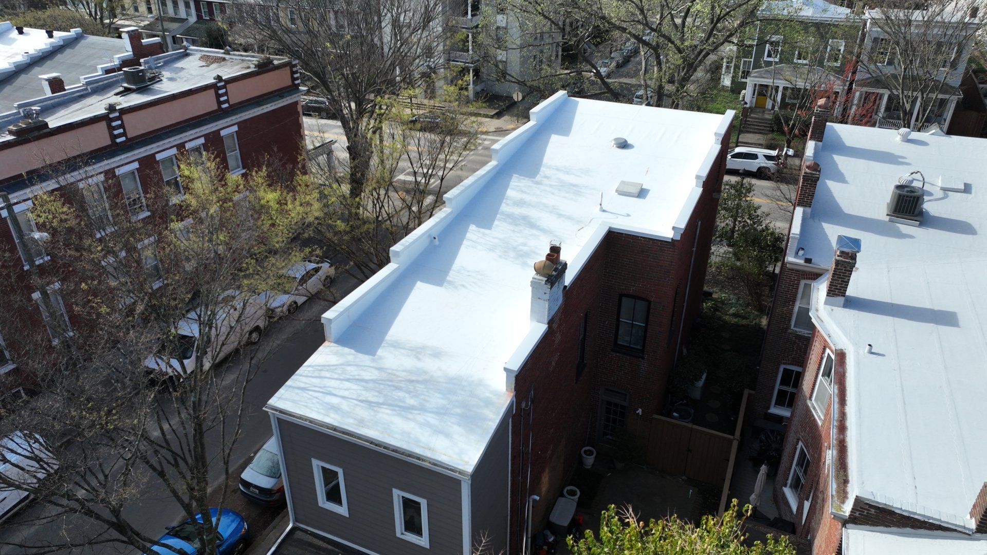 Aerial view of urban rooftop with white membrane covering a brick building surrounded by other structures and bare trees