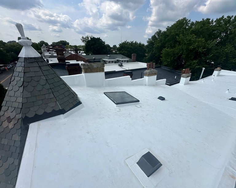 Flat white commercial rooftop with HVAC units, vents, and gray shingled peak, overlooking residential area with trees