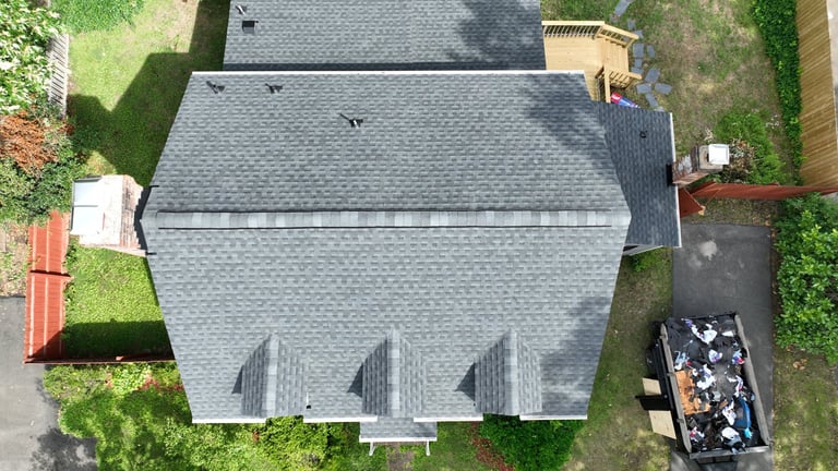 Aerial view of a house with gray shingled roof surrounded by green lawn and neighboring properties