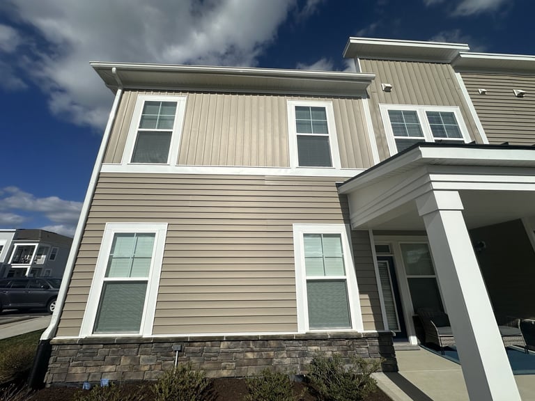 Modern two-story house with beige siding, white trim, and multiple windows against a blue sky