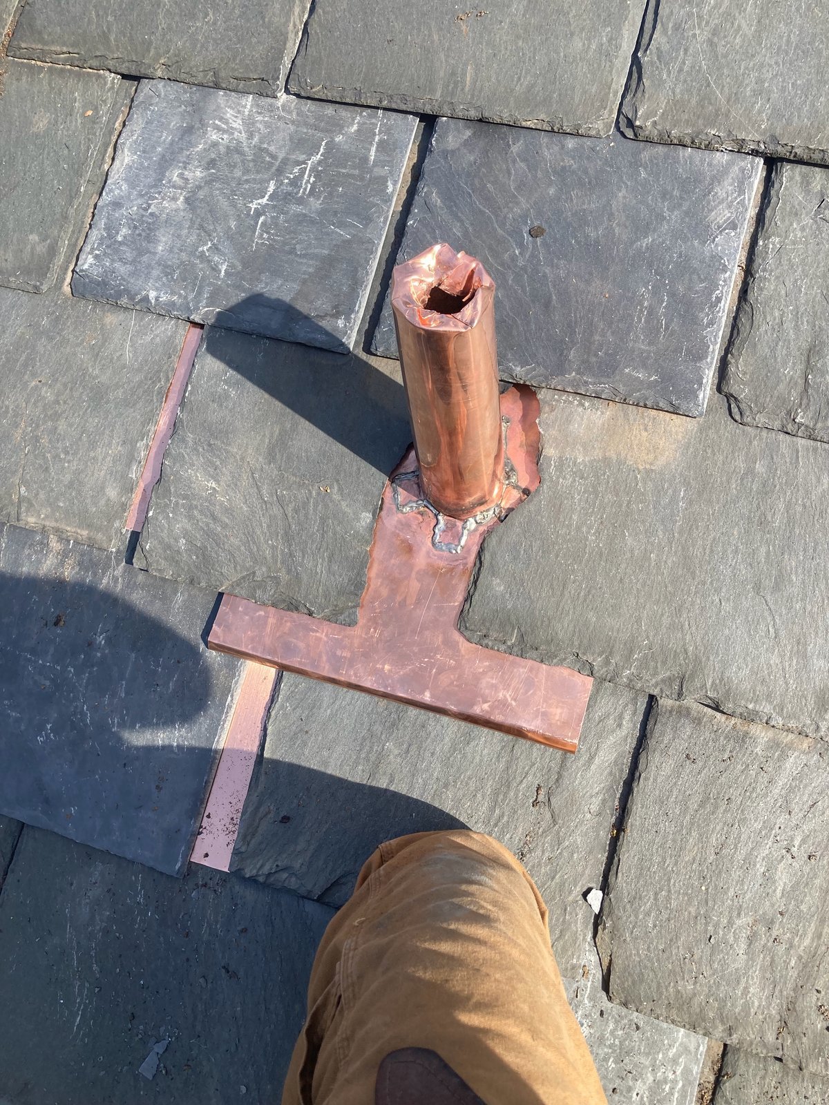 Soldered copper vent pipe flashing installed on a gray slate roof
