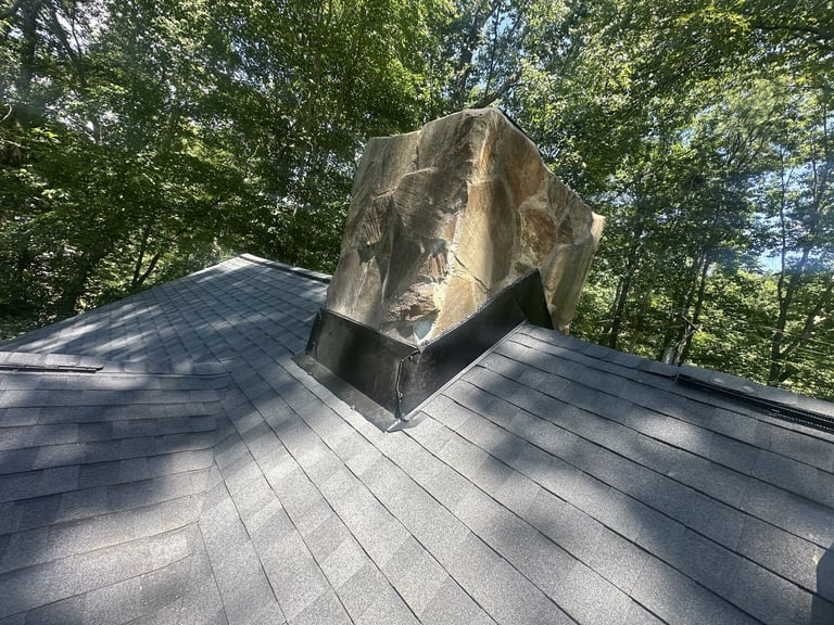 Black metal flashing around a stone chimney on a shingle roof