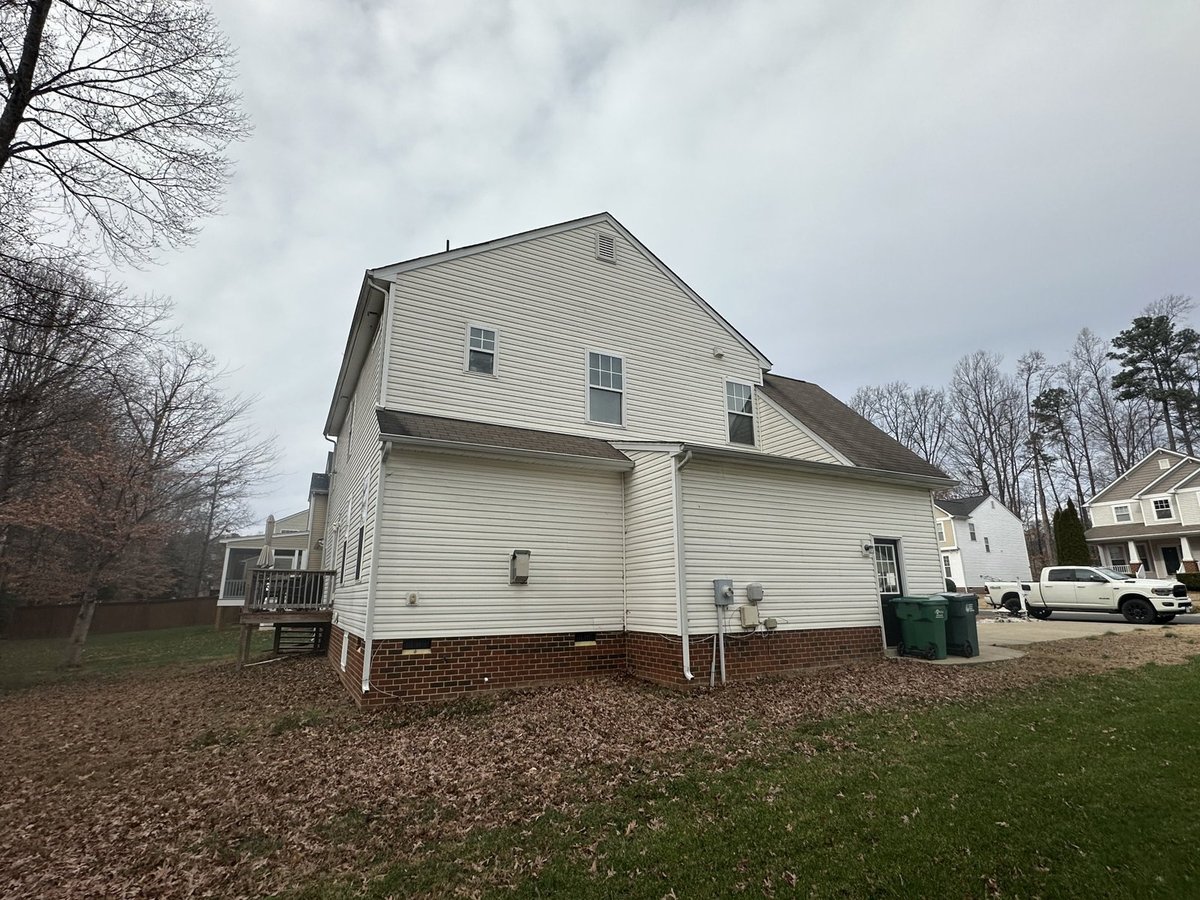White two-story house with brick foundation on residential lot with bare trees and driveway