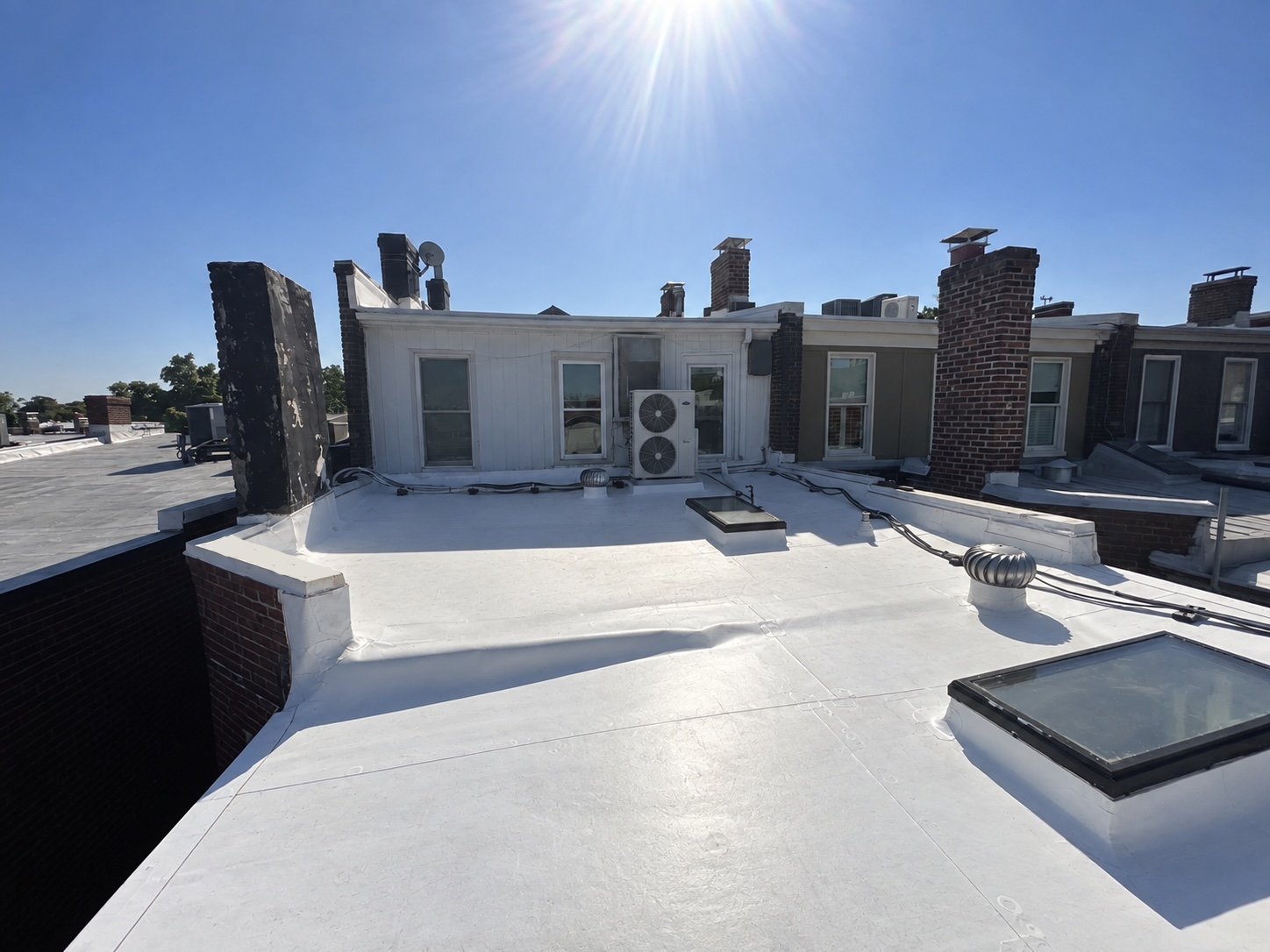 Rooftop with white surface, HVAC units, brick chimneys, and solar panels under clear blue sky