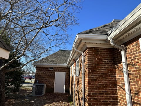 Brick house exterior with white gutters and trim under clear blue sky on a sunny day