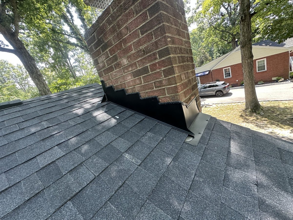 Black step and counter flashing around a brick chimney on a shingle roof