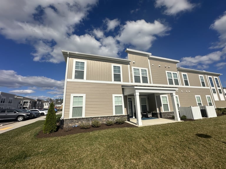 Modern tan and cream townhouse with multiple units, front lawn, and blue sky with white clouds